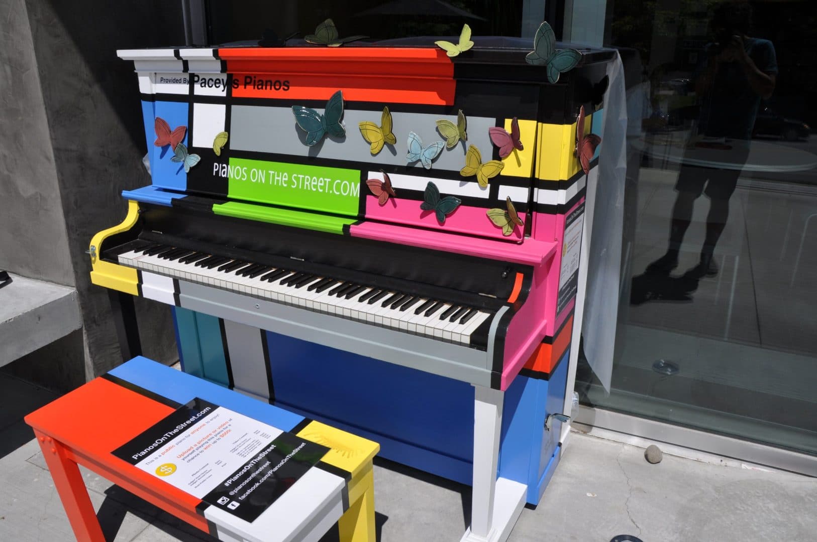 A Mondrian-style piano in bold colour blocks, crawling with ceramic butterflies, with its matching bench.