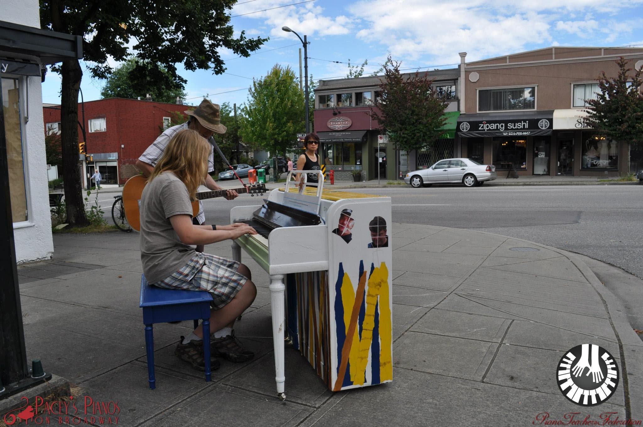 A duo busks on a corner near Main Street with a ribbon-striped piano and an acoustic guitar.