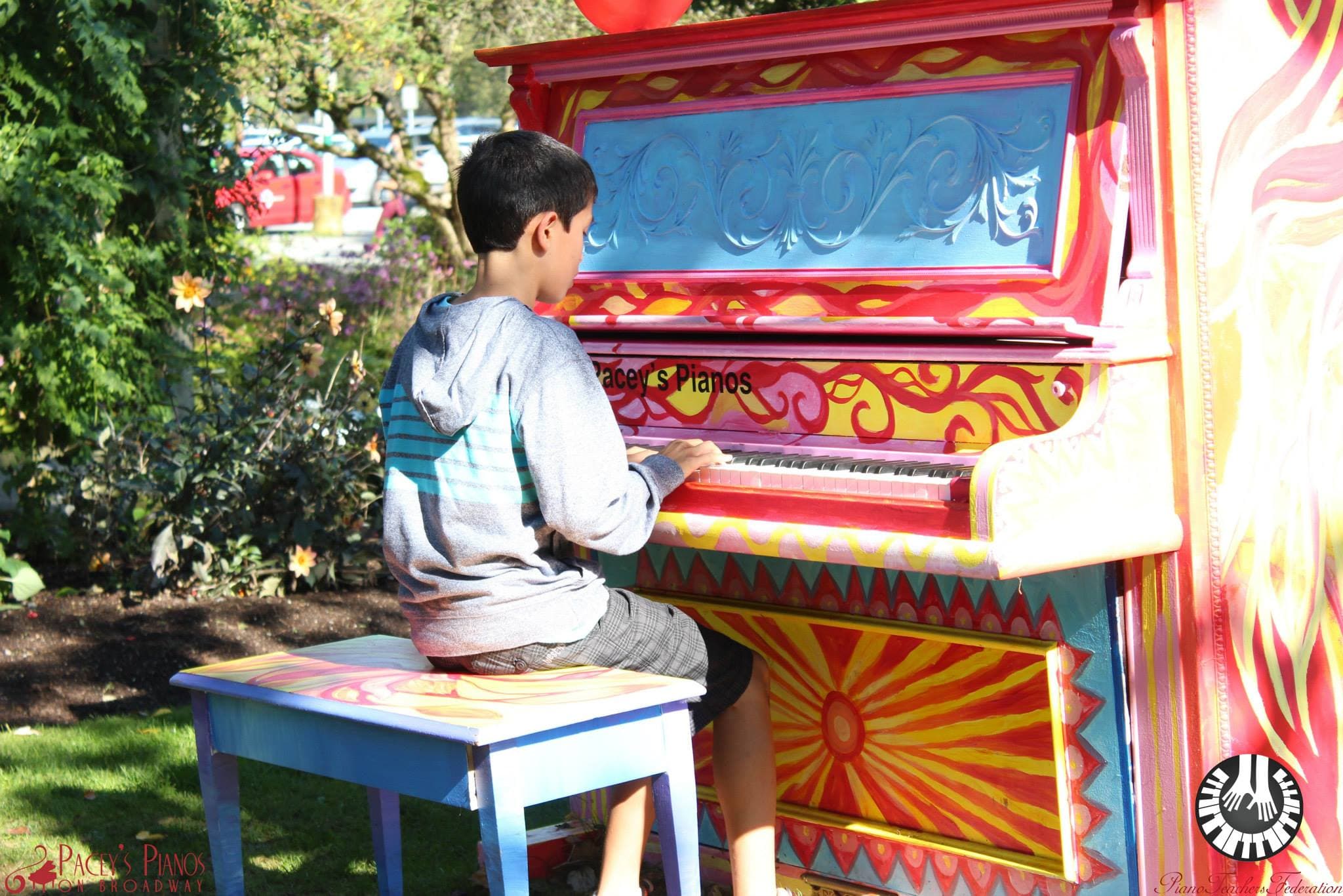 A boy plays a flame-red sunburst piano in golden afternoon sun, a red balloon bobbing on the piano top.