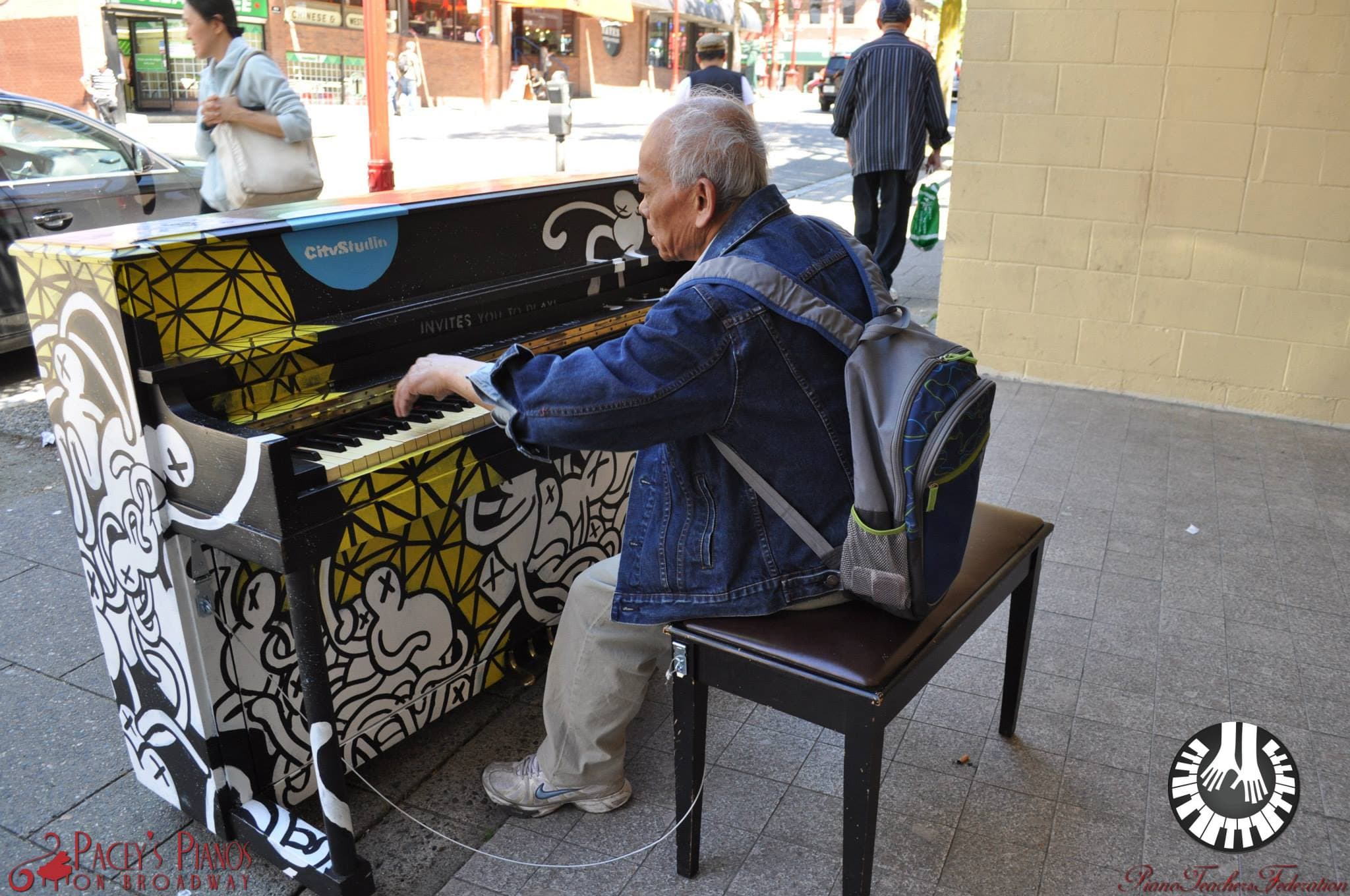 Backpack still on, an elderly man reaches over the bench to try the doodle piano on a Chinatown sidewalk.