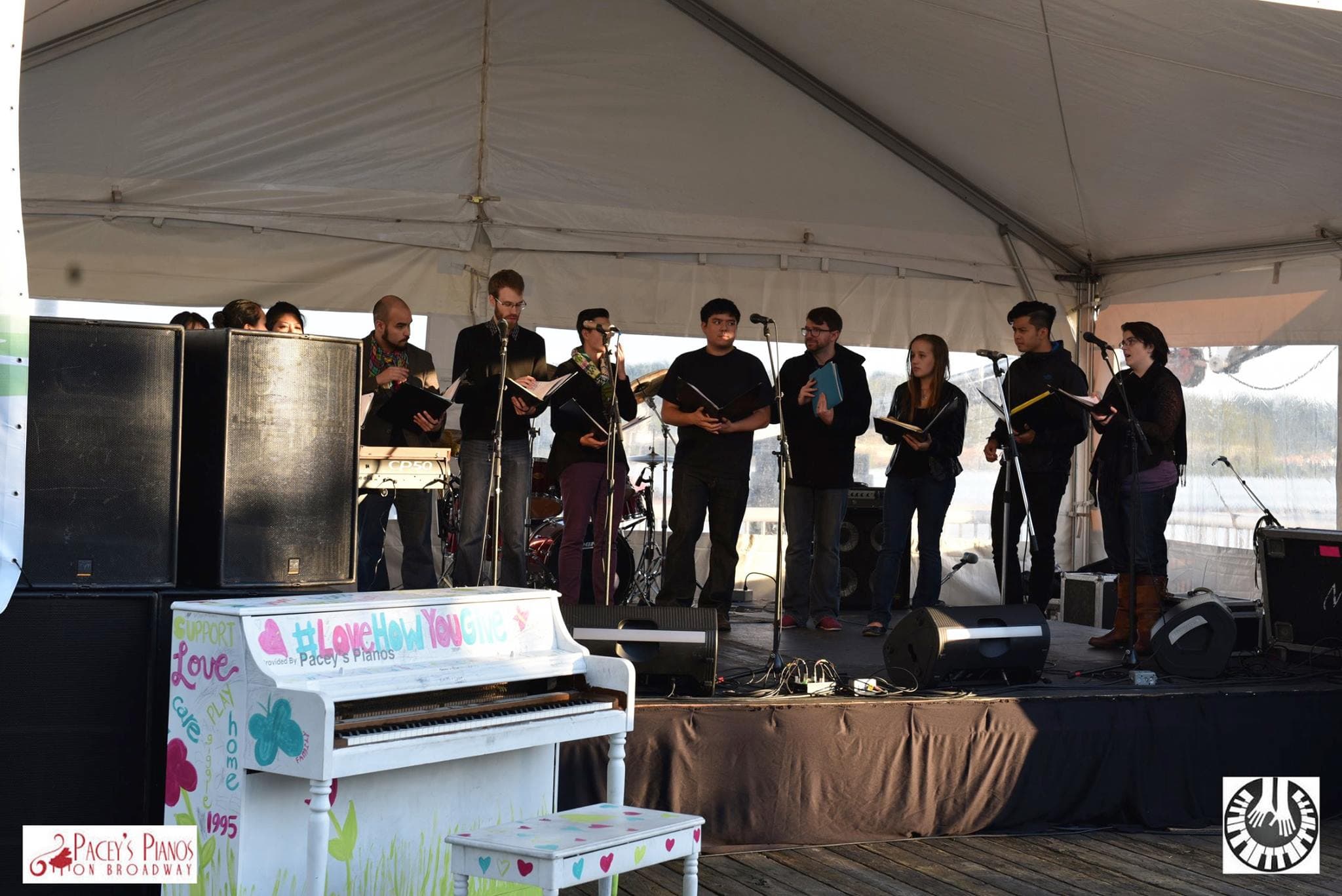 A white piano hand-lettered #LoveHowYouGive waits stage-side while a young choir performs.