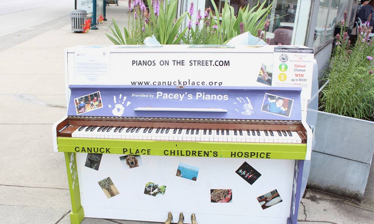 The Canuck Place Children's Hospice piano with purple fallboard, lime trim, and snapshots of kids, among tall liatris planters.