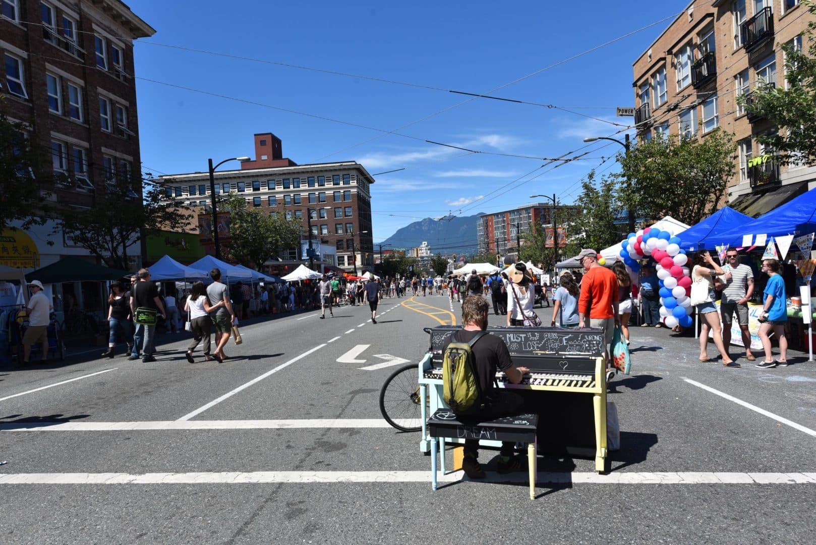 A lone player at an upright in the middle of a car-free Main Street, festival tents and mountains down the avenue.
