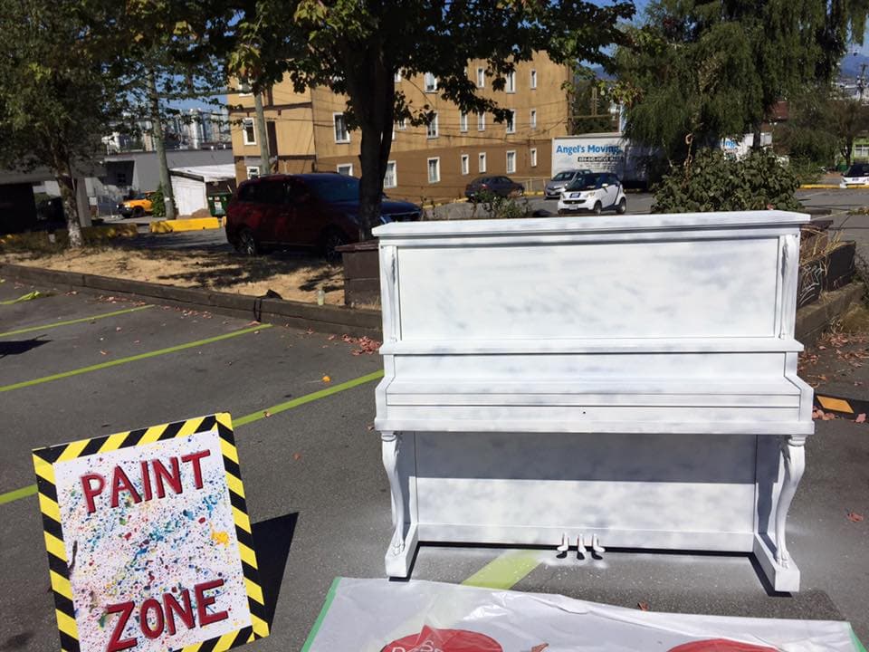 A freshly primed all-white upright waits in a parking-lot Paint Zone, a blank canvas before the artists arrive.